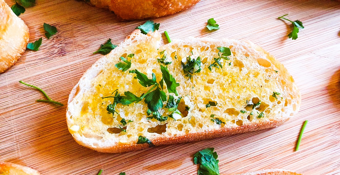 Slice of garlic bread with fresh herbs on a wooden board