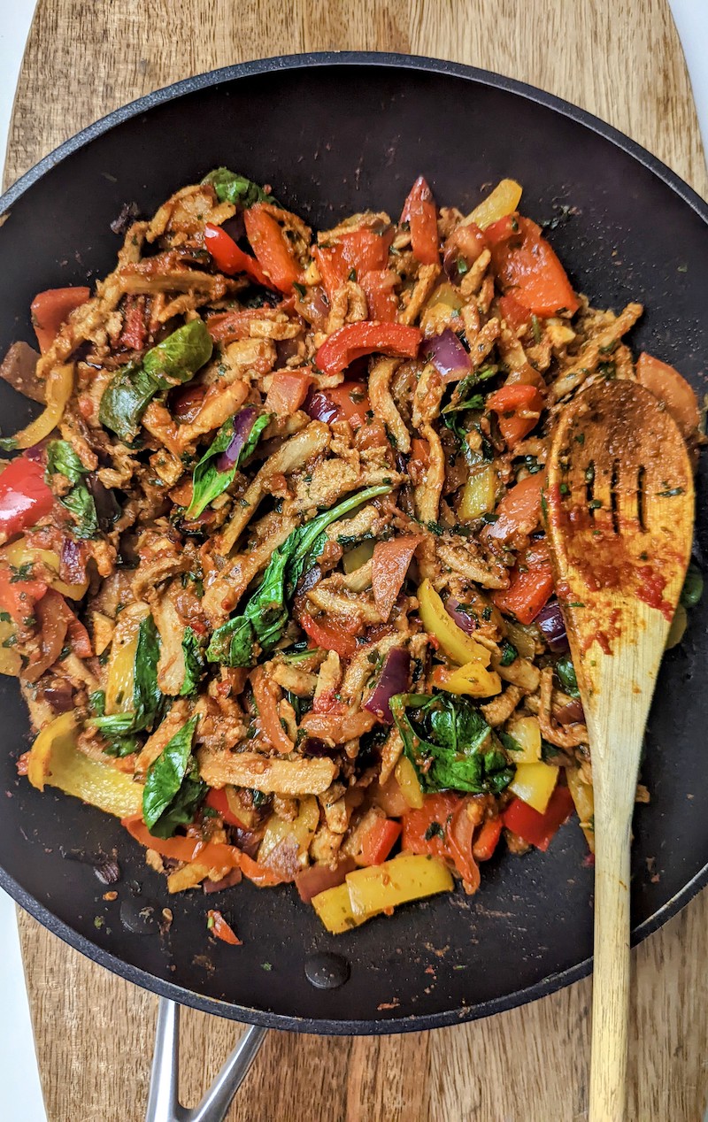 vegetables and plant shawarma in a frying pan with a wooden spoon