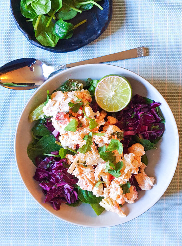 creamy baked cauliflower with red cabbage, spinach and lime wedge in a bowl on a blue background