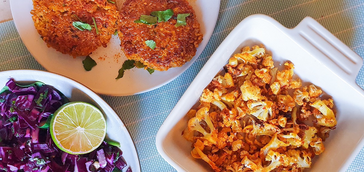 roasted cauliflower in a square dish with sweet potato fritters in a plate, both on a blue backgroun