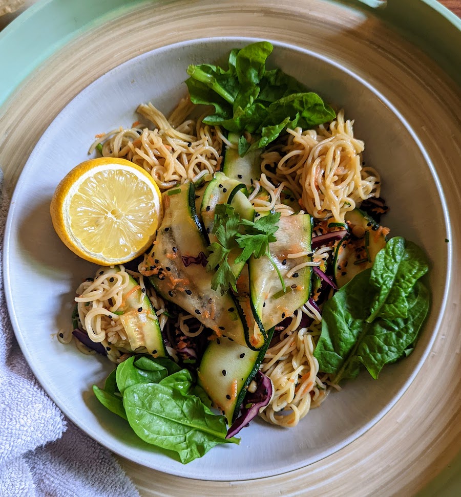 ribboned courgette with noodles and a wedge of lemon placed in a bowl on a tray