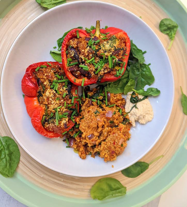 two quinoa stuffed peppers halves with hummus in a large bowl on a wooden tray with spinach leaves