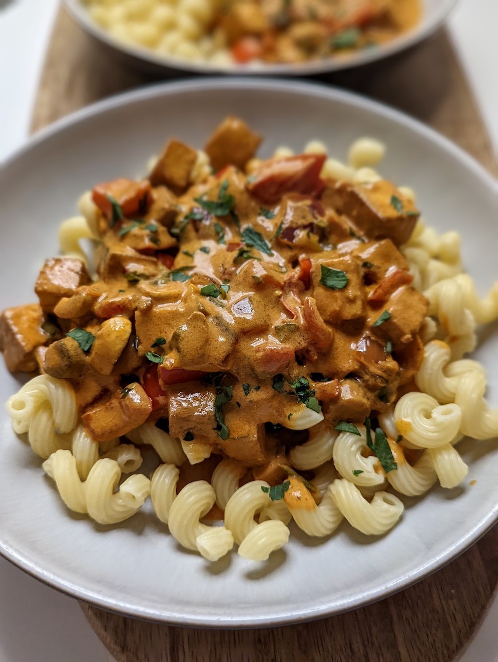 tofu in a turmeric sauce on spiralli pasta in a white bowl on a wooden board